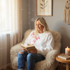 Woman in Darling Details Top reading a book in a cozy living room with sequin bowknot details.