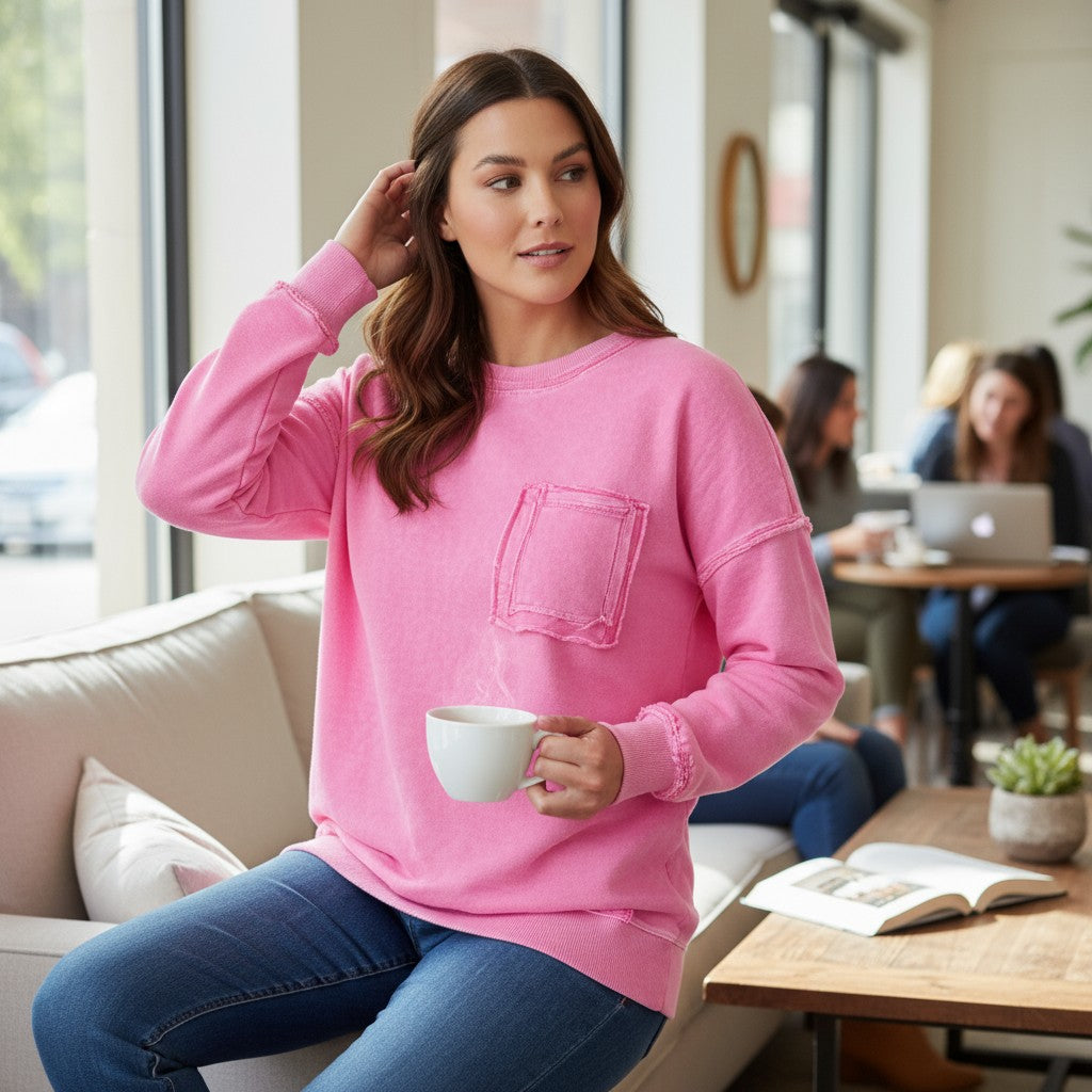 Woman wearing a pink Cloud Nine Crew pullover while enjoying a coffee in a cozy café setting.