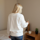 Back view of a woman wearing the DARLING DETAILS TOP, a cozy white oversized sweatshirt styled with casual jeans.