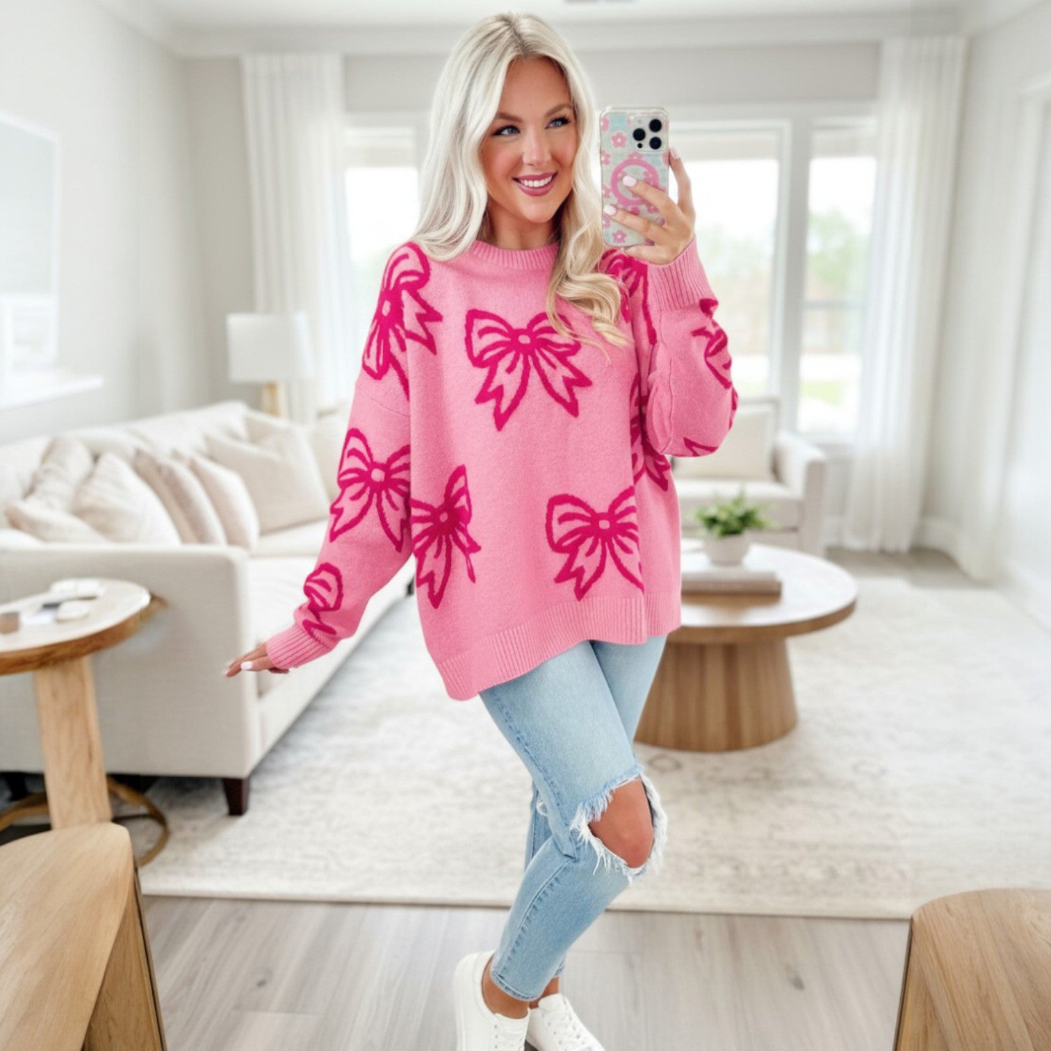 Young woman in a pink RIBBON ROMANCE SWEATER with bow patterns, smiling in a bright living room.