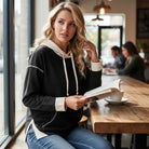 Woman wearing a MODERN EDGE HOODIE, reading a book in a cozy cafe with a stylish atmosphere.