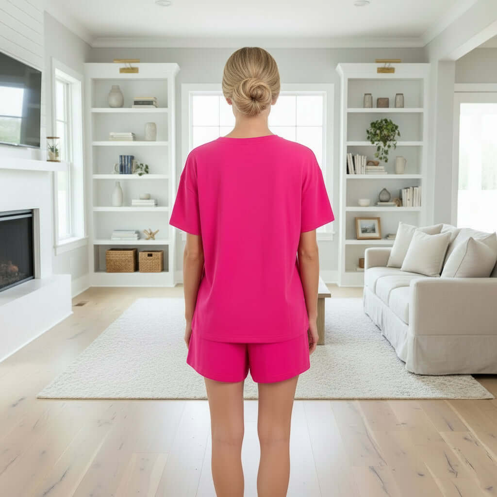 Model wearing CORE COMFORT SHORTS SET (hot pink) featuring a short sleeve top and shorts in a cozy living room.