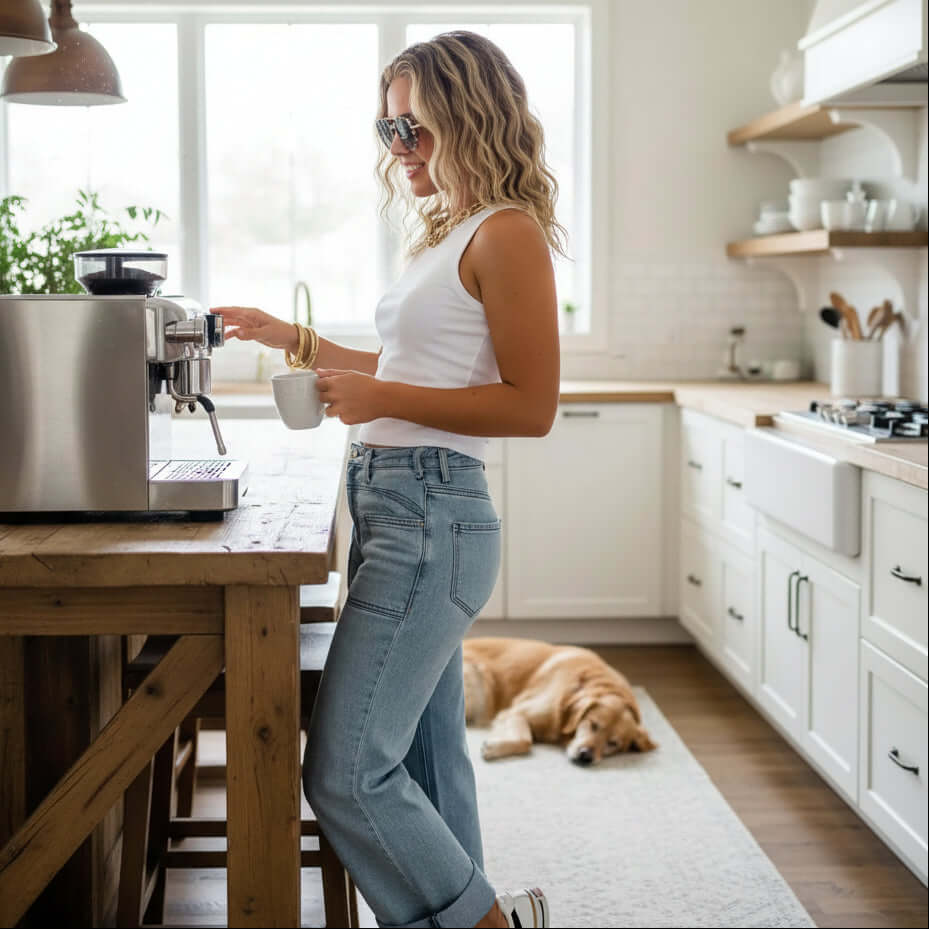 Woman in BLAKELY CLOVER FRONT POCKET JEANS making coffee in stylish kitchen, golden retriever resting nearby.