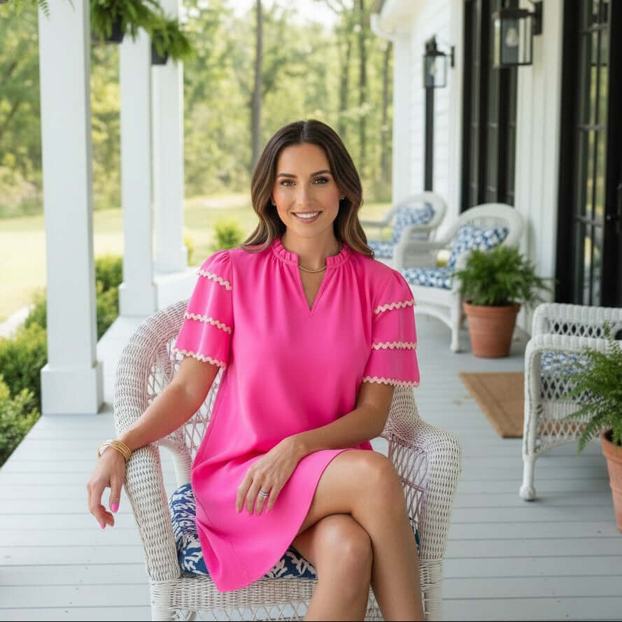 Model wearing the Kersten Ric Rac Dress, Hot Pink, showcasing ruffle sleeves on a porch.