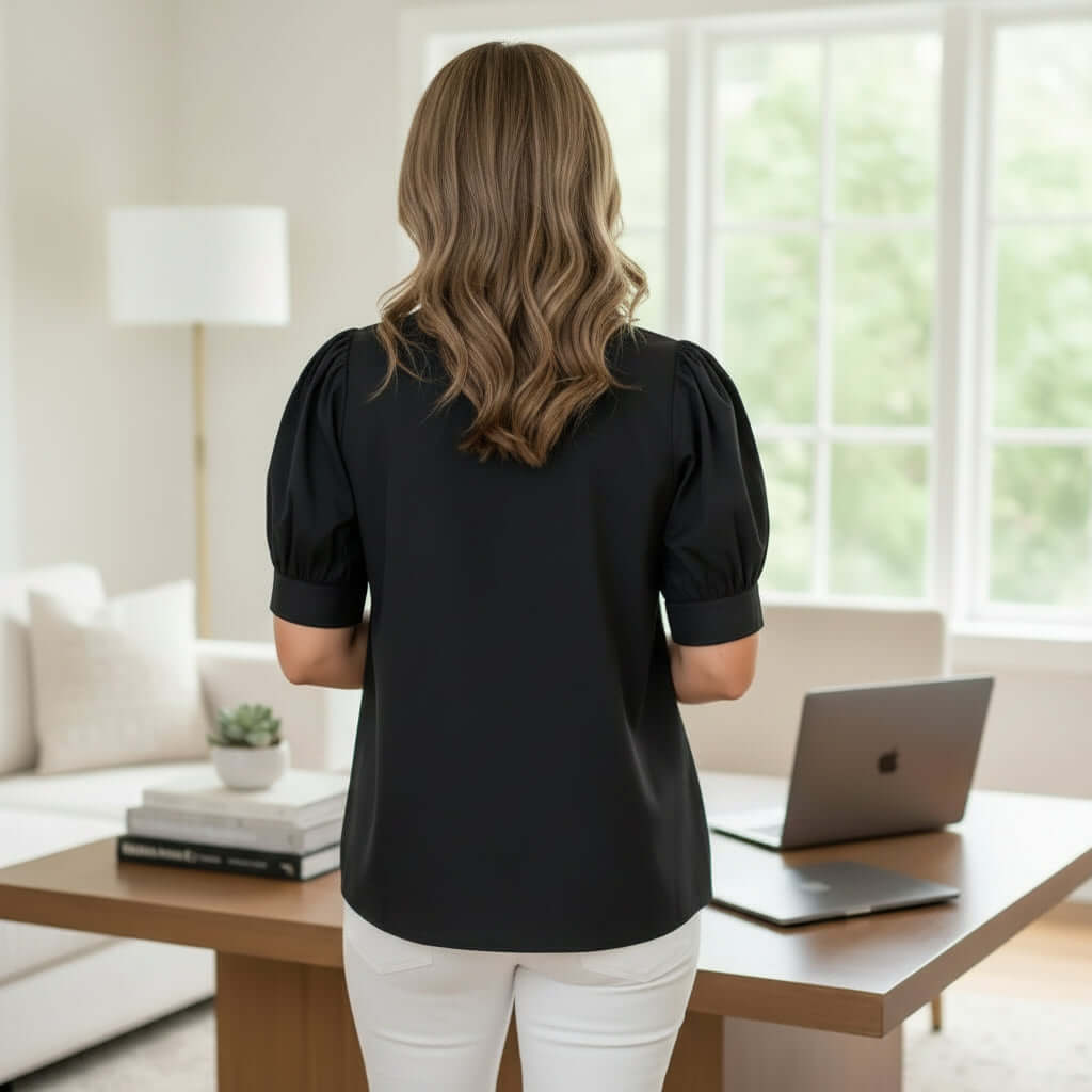 Back view of a woman wearing the STRUCTURED GRACE TOP, a tailored black blouse with puff sleeves.