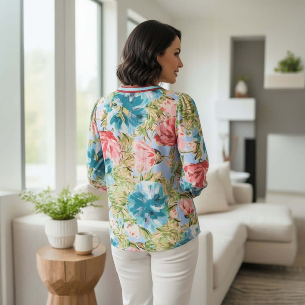 TEMPLATE TOP (long sleeve) featuring a vibrant floral design, styled with white pants in a modern living space.
