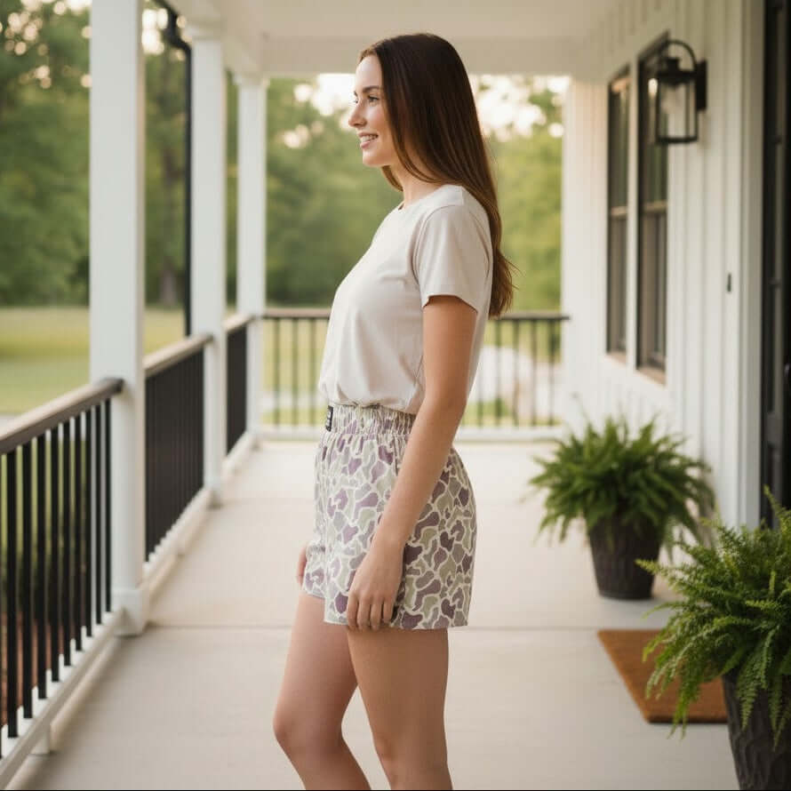 Woman wearing LULU MAC ACTIVE SHORTS- Camo on a porch in a stylish casual setting, showcasing sporty comfort.