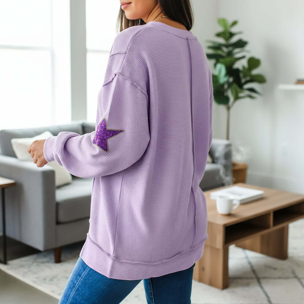 Back view of a woman wearing a lavender MARDI GRAS STAR PULLOVER with sequined star patch.