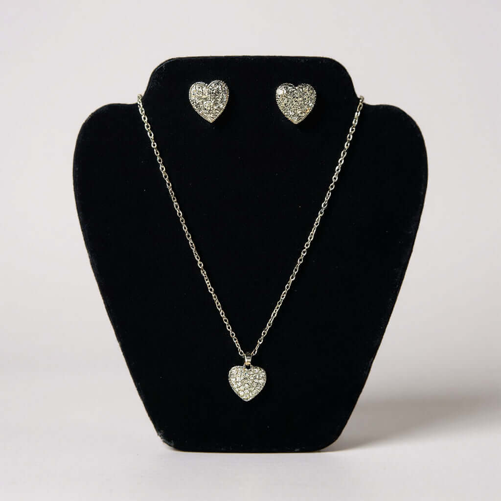 LOVE STORY Earrings and Necklace Set (silver) displayed on a black jewelry stand, featuring heart-shaped designs.