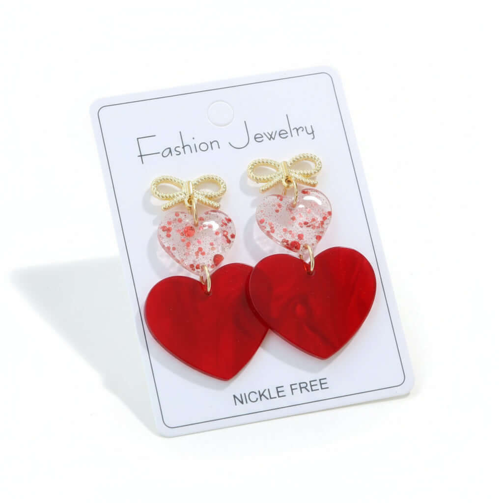 CHERISHED HEARTS EARRING featuring red acrylic heart drops and gold-tone bow stud on a display card.