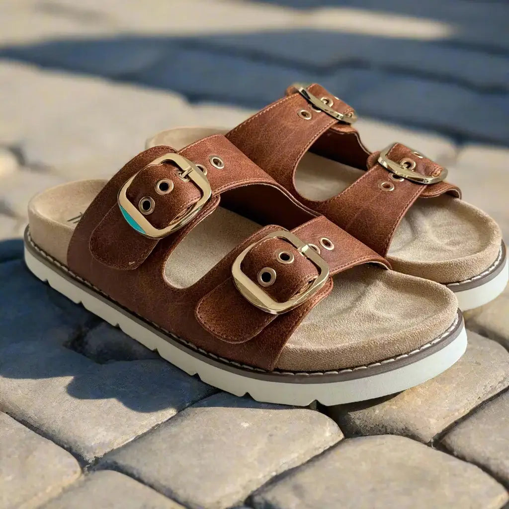 Feelin' Saucy sandals by Corkys with adjustable straps and gold buckles on a textured background.