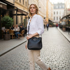 Model showcasing the POLISHED PATH HANDBAG (black) while strolling down a charming street.
