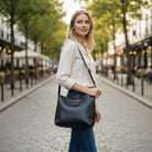 Model showcasing the POLISHED PATH HANDBAG (black) while strolling in a picturesque street, embodying elegant style.