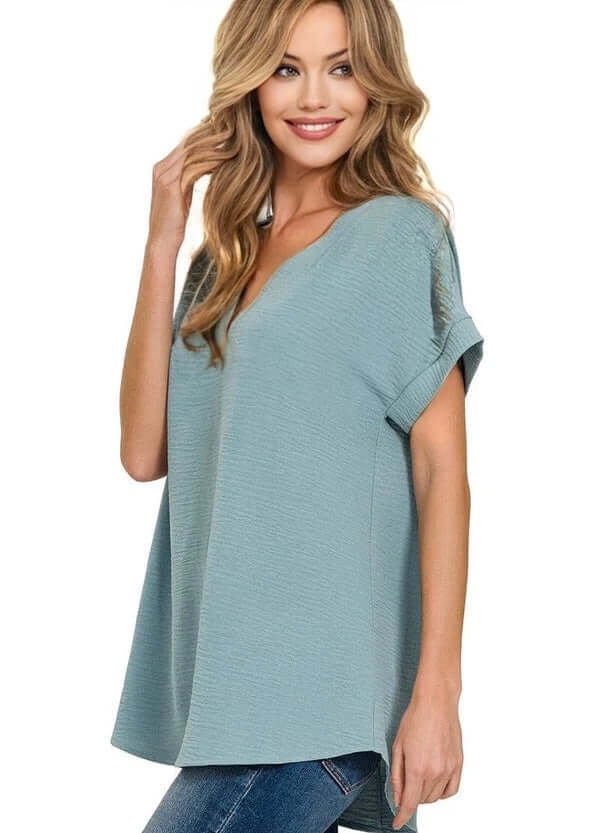 Woman in dusty blue Zenana Air Kiss Top with V-neck, showcasing modern high-low hem style and relaxed fit.