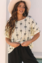 Model wearing Ribbons in the Sand top with bow patterns, smiling and dressed in a stylish summer outfit.