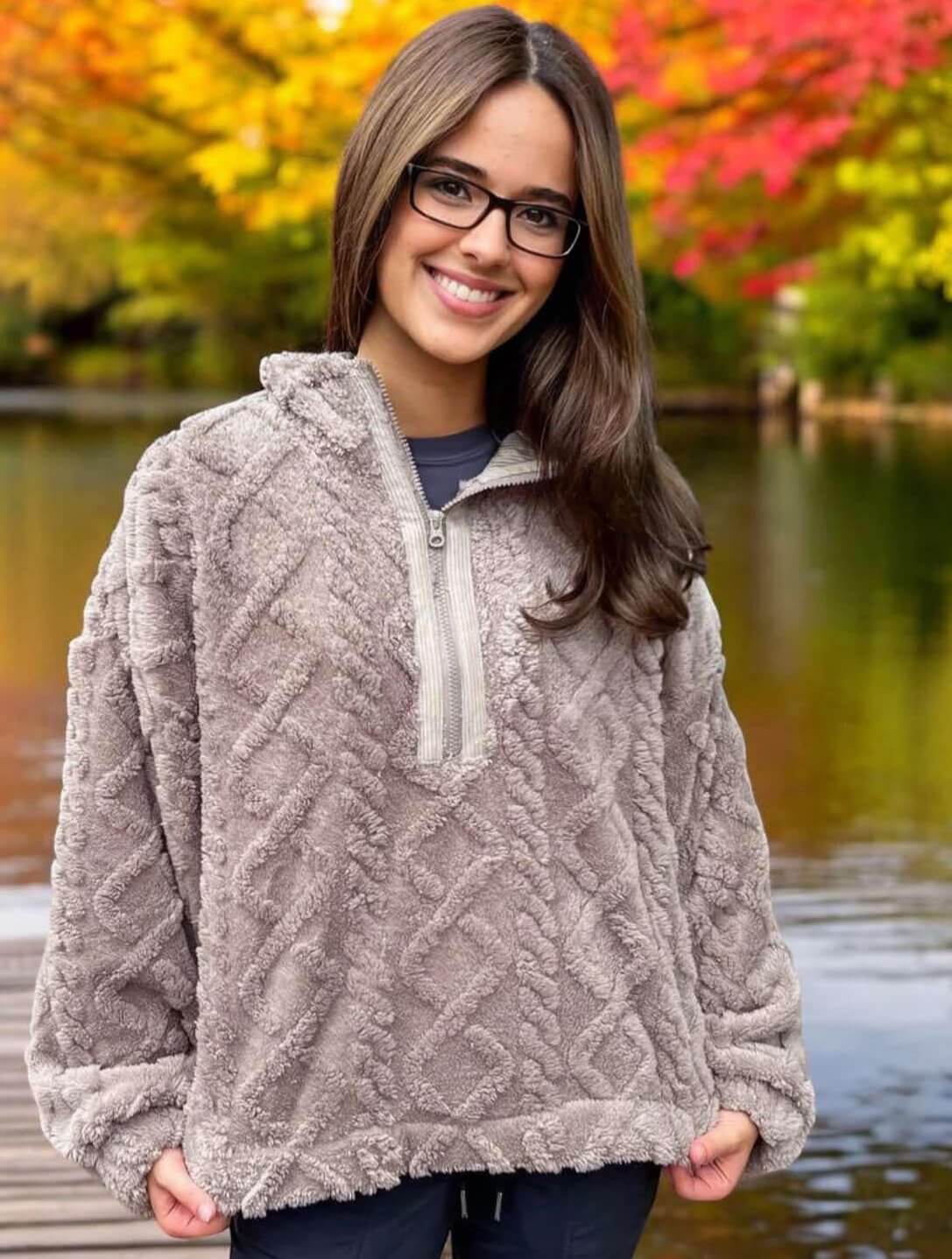 Woman wearing charcoal Teddy Bear Sherpa fleece pullover with cable pattern by a lake with autumn trees in the background.