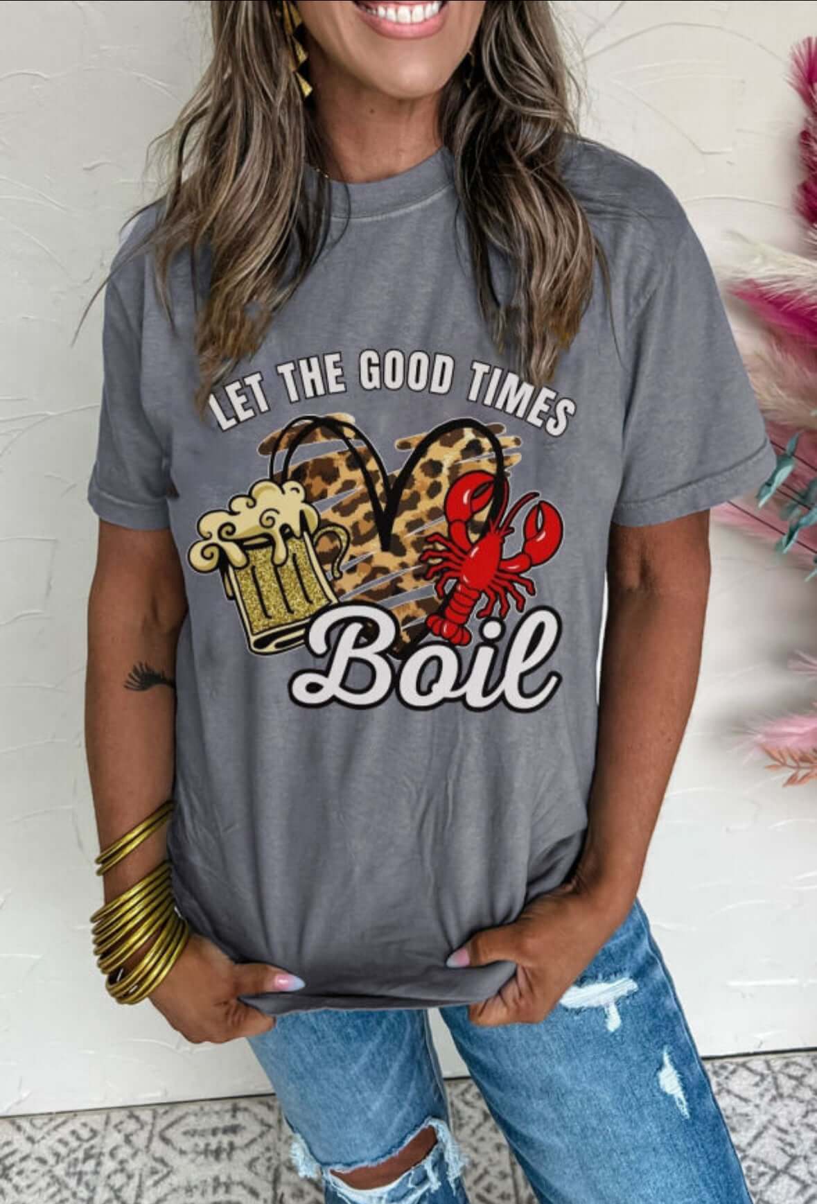 Woman wearing 'Let the Good Times Boil' graphic tee with crawfish, beer mugs, and leopard heart design.