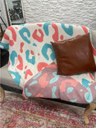 Cozy Dixie Bella Heavenly Aire throw blanket with vibrant leopard print on a sofa, alongside a brown decorative pillow.