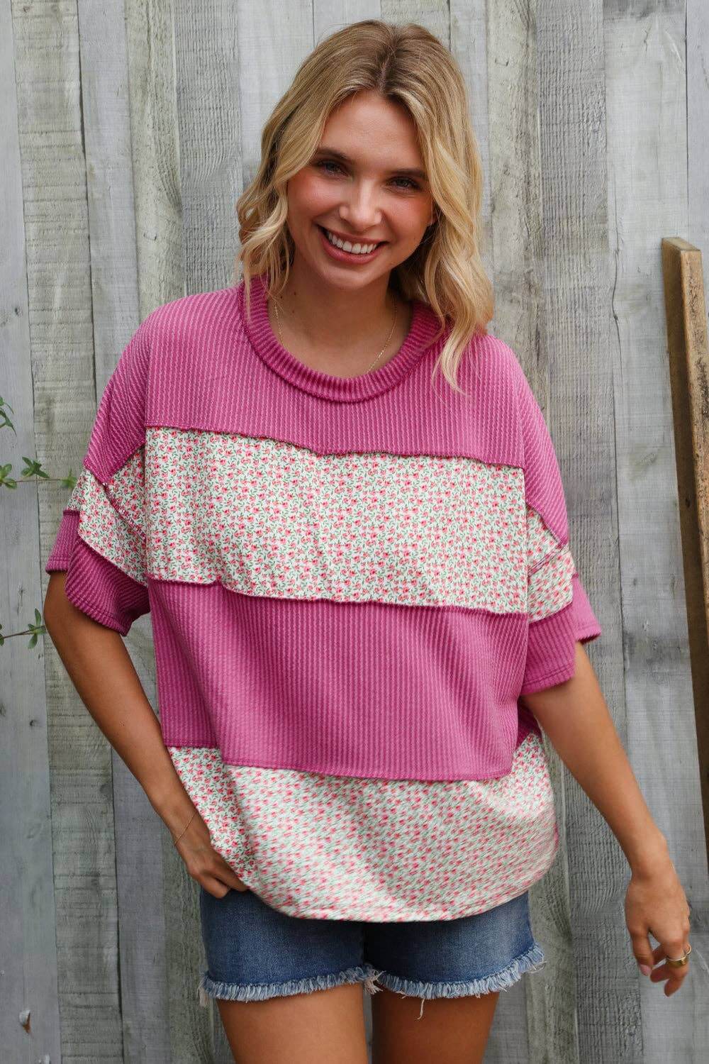 Fuchsia floral color block pullover with wavy rib knit, short sleeves, styled casually with denim shorts.