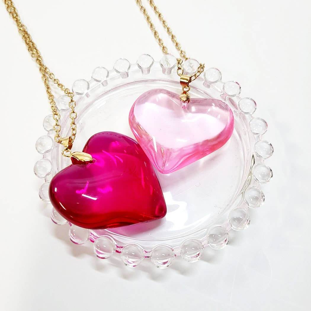 Assorted heart-shaped pendant necklaces in pink and red on a decorative glass plate, perfect for Valentine's Day gifts.