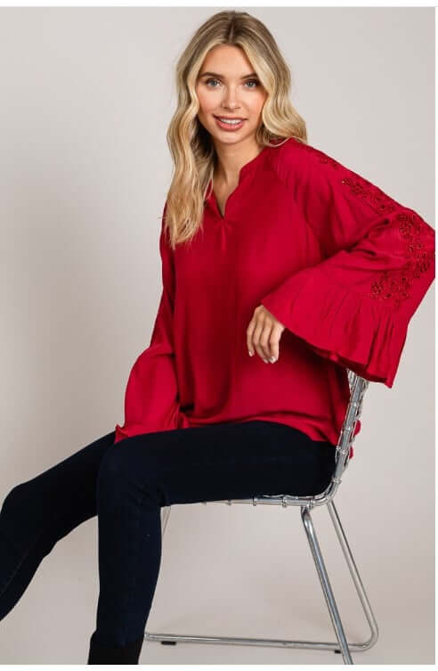 Woman wearing VIP ACCESS red top with bell sleeves and eyelet detailing from Cotton Blue.