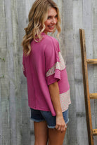 Woman in fuchsia floral dolman pullover with color block design, styled with denim shorts, outdoors.
