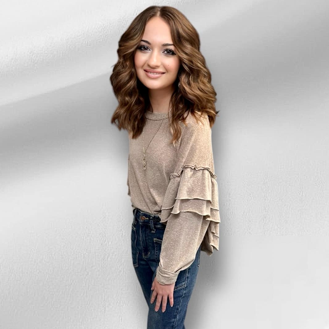 Woman wearing Soft Landing Top in neutral tan with double ruffle details and exposed back seam, styled with jeans.