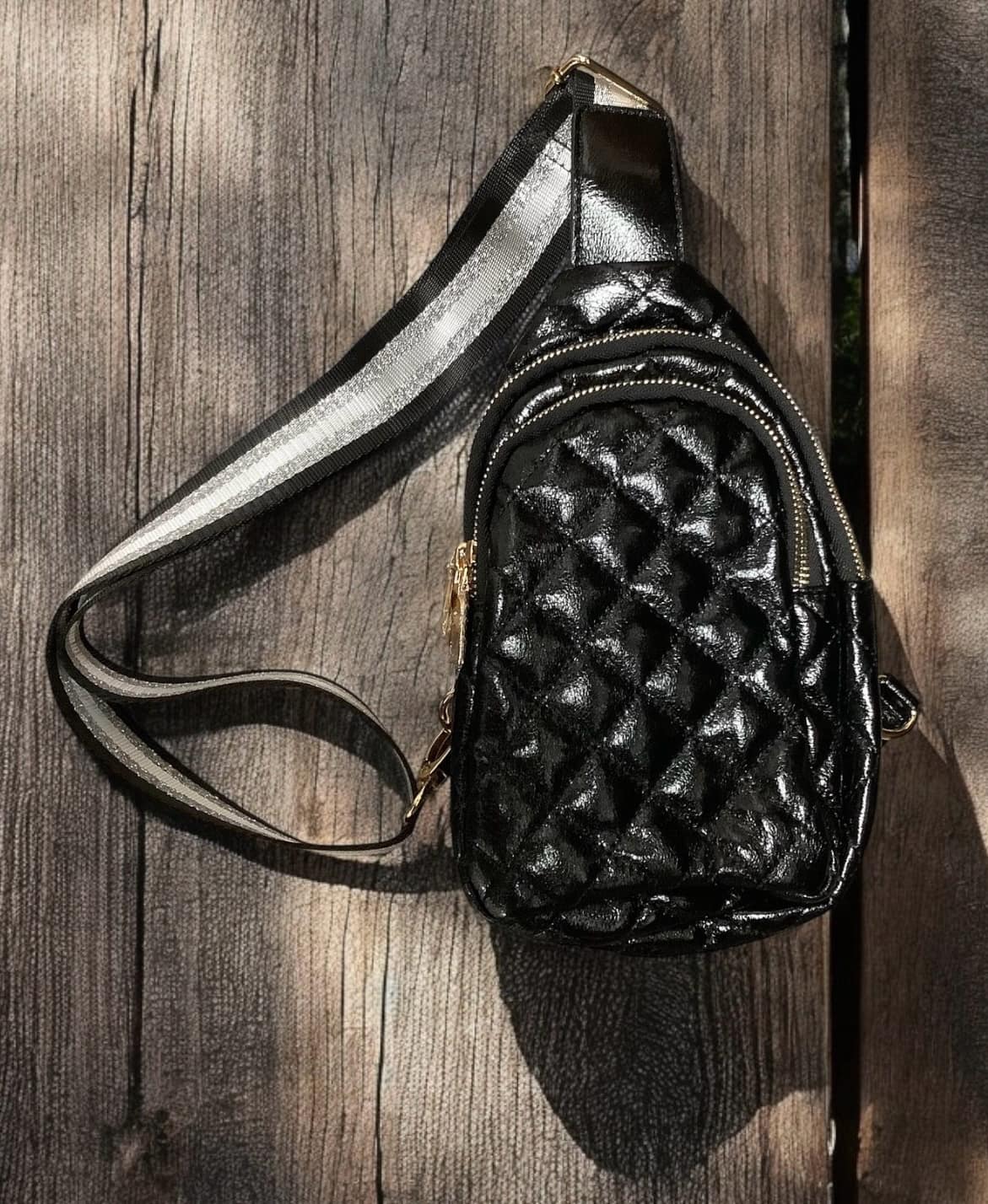 Downtown Shopper Sling Bag in quilted black design with adjustable strap resting on wooden surface.