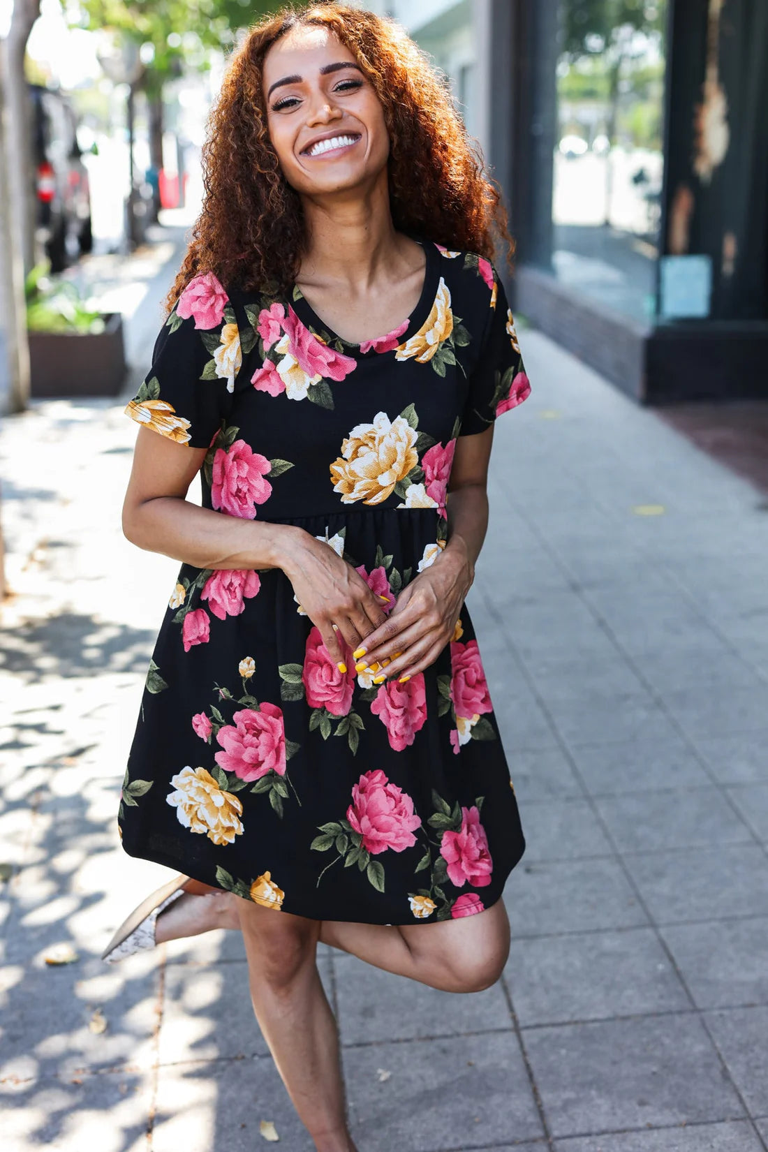 Smiling model wearing the Twilight Garden Party Dress with floral patterns, outdoors on a sunny day.