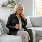 WARM IMPRESSIONS BUTTON DOWN shacket in black worn by a woman holding a coffee cup while sitting comfortably on a sofa.