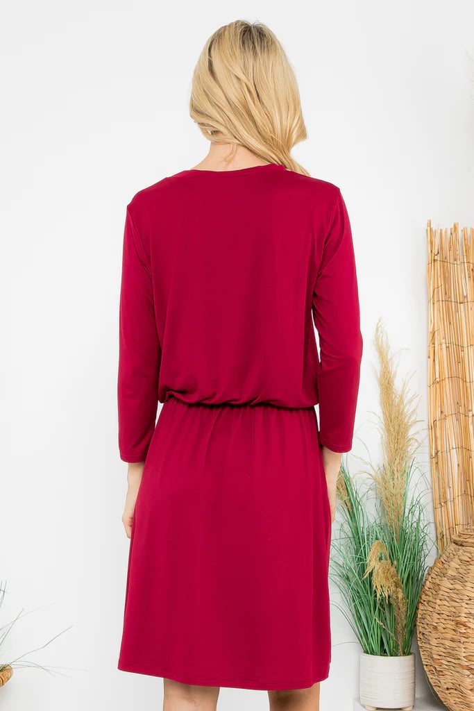 Woman wearing a red Wine and Dine Dress with 3/4 sleeves and cinch waist, shown from the back, highlighting stylish knee-length design.