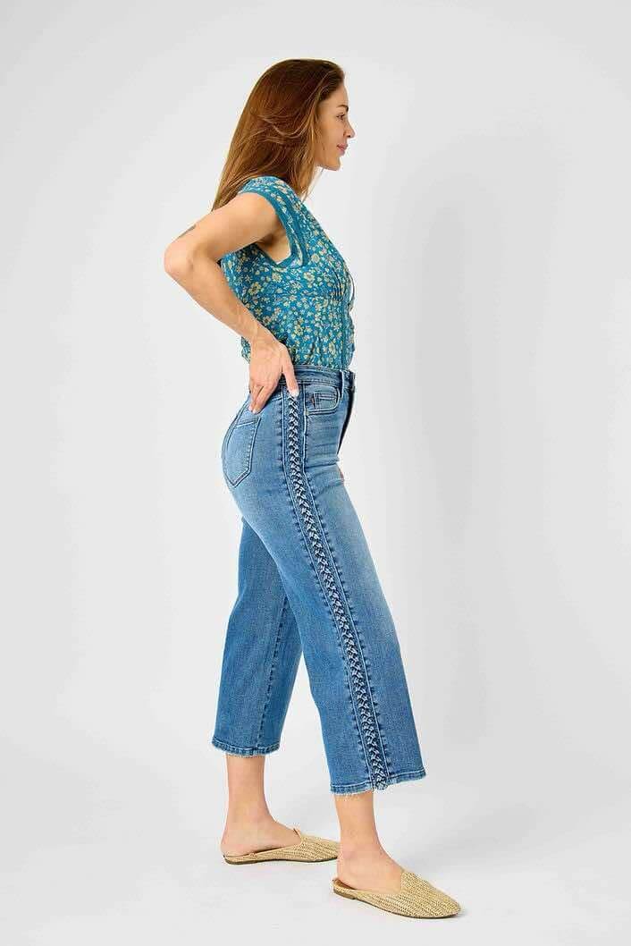 Woman wearing Judy Blue Braided Betty Jeans with unique side braid detail and wide leg design, showcasing trendy fashion statement.