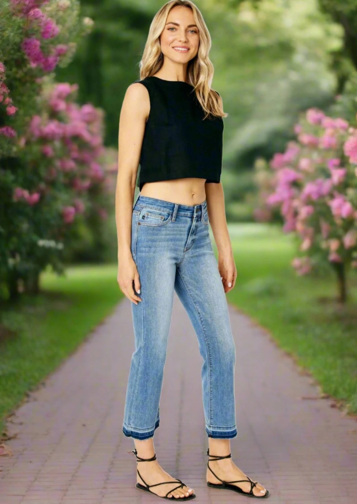 Model wearing JUDY BLUE Amelia Jeans with a cropped top, standing on a floral path, showcasing a stylish midrise fit.