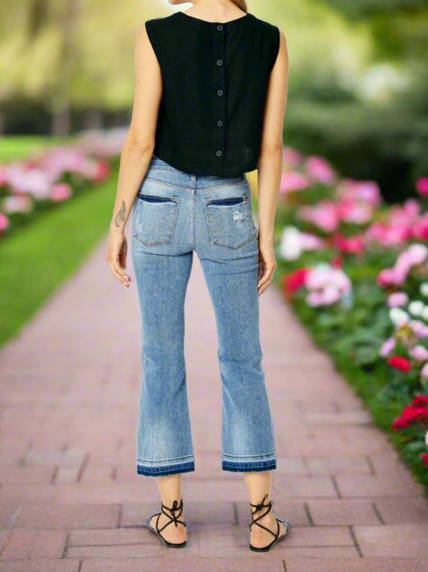 Back view of a model wearing Judy Blue Amelia Jeans with cropped bootcut and a stylish black top in a garden setup.