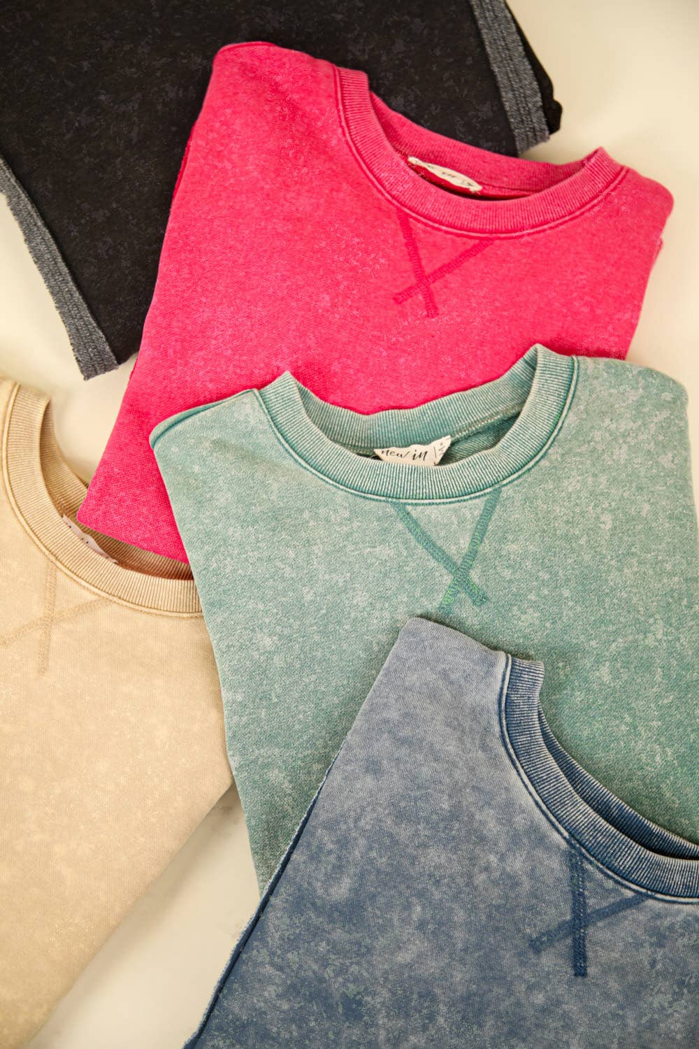 A collection of oversized crewneck tops in various colors, including pink, green, beige, and blue, showcasing mineral-washed fabric.