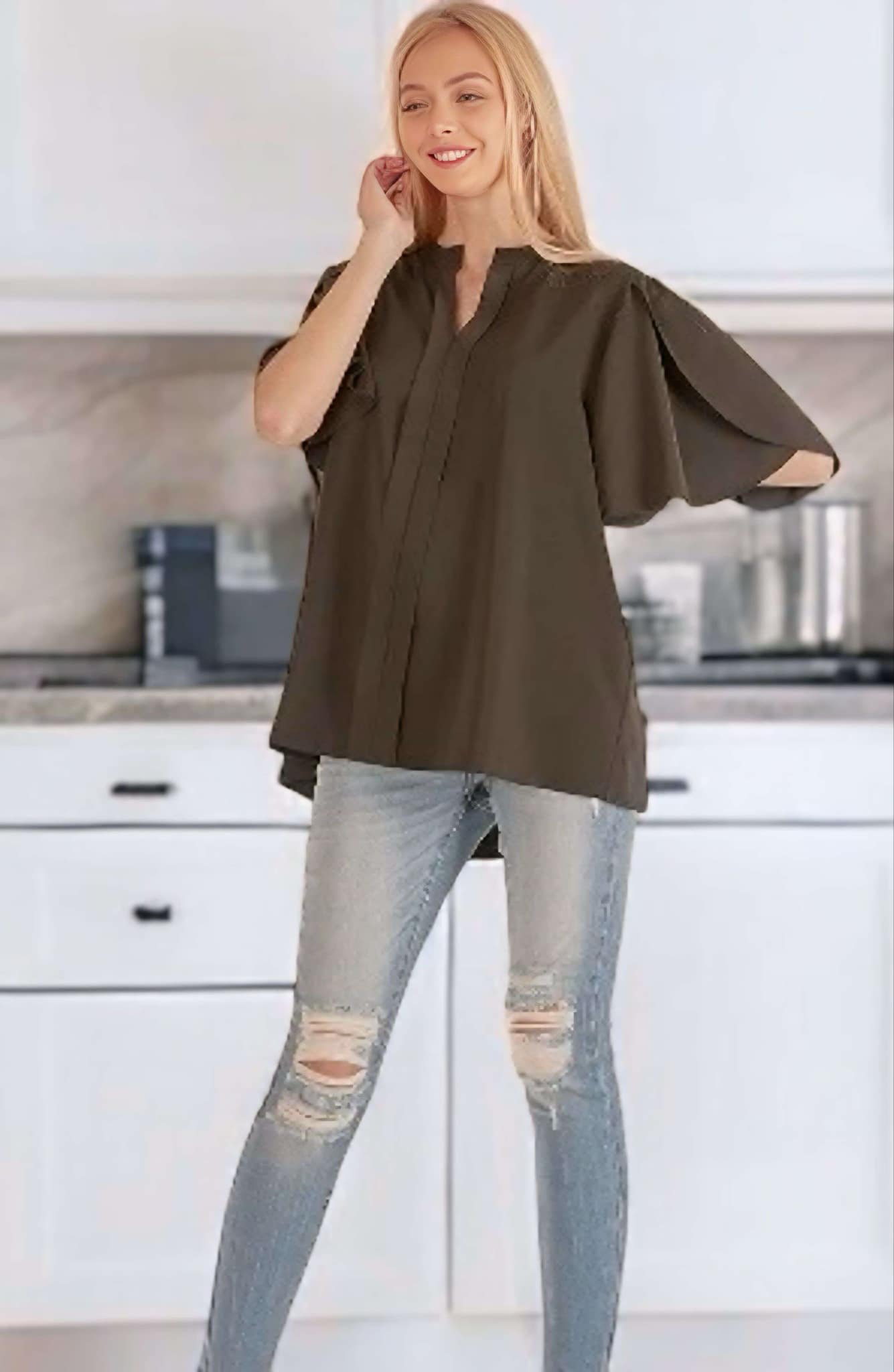 Black loose blouse with petal flutter sleeves paired with ripped jeans in a modern kitchen setting.