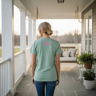 Woman wearing LULU MAC- OCD TEE IN DUSTY MINERAL WASH BLUE, showing back design on a porch.