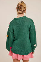 Woman wearing dark green square up sweater with 3D crocheted flowers and pink skirt, showcasing boho style from the back.