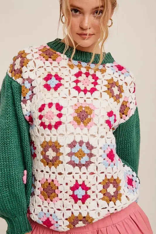 Woman wearing handmade floral patchwork square sweater with 3D crocheted flowers, featuring green sleeves and vibrant colors.