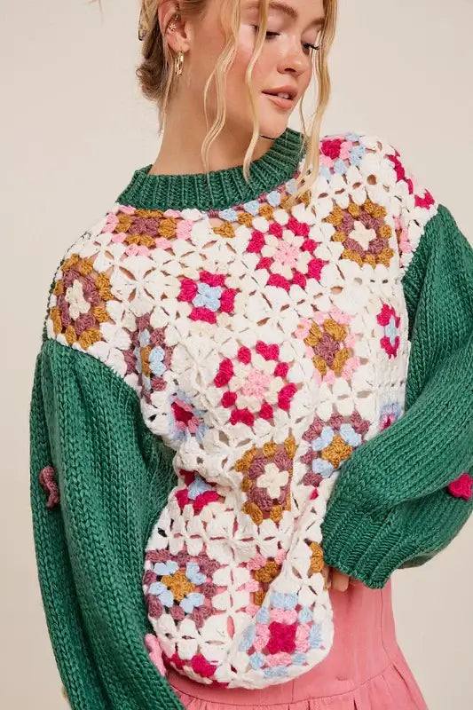 Woman wearing a boho SQUARE UP SWEATER with floral patchwork and 3D flowers, featuring a mix of green, pink, blue, and cream colors.