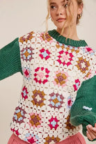 Floral patchwork sweater with 3D crocheted flowers, dark green sleeves, and ribbed neckline, worn by a woman.