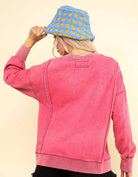 Woman wearing an oversized pink Flex Time Crew Neck with stylish stitch details and a blue crochet bucket hat.