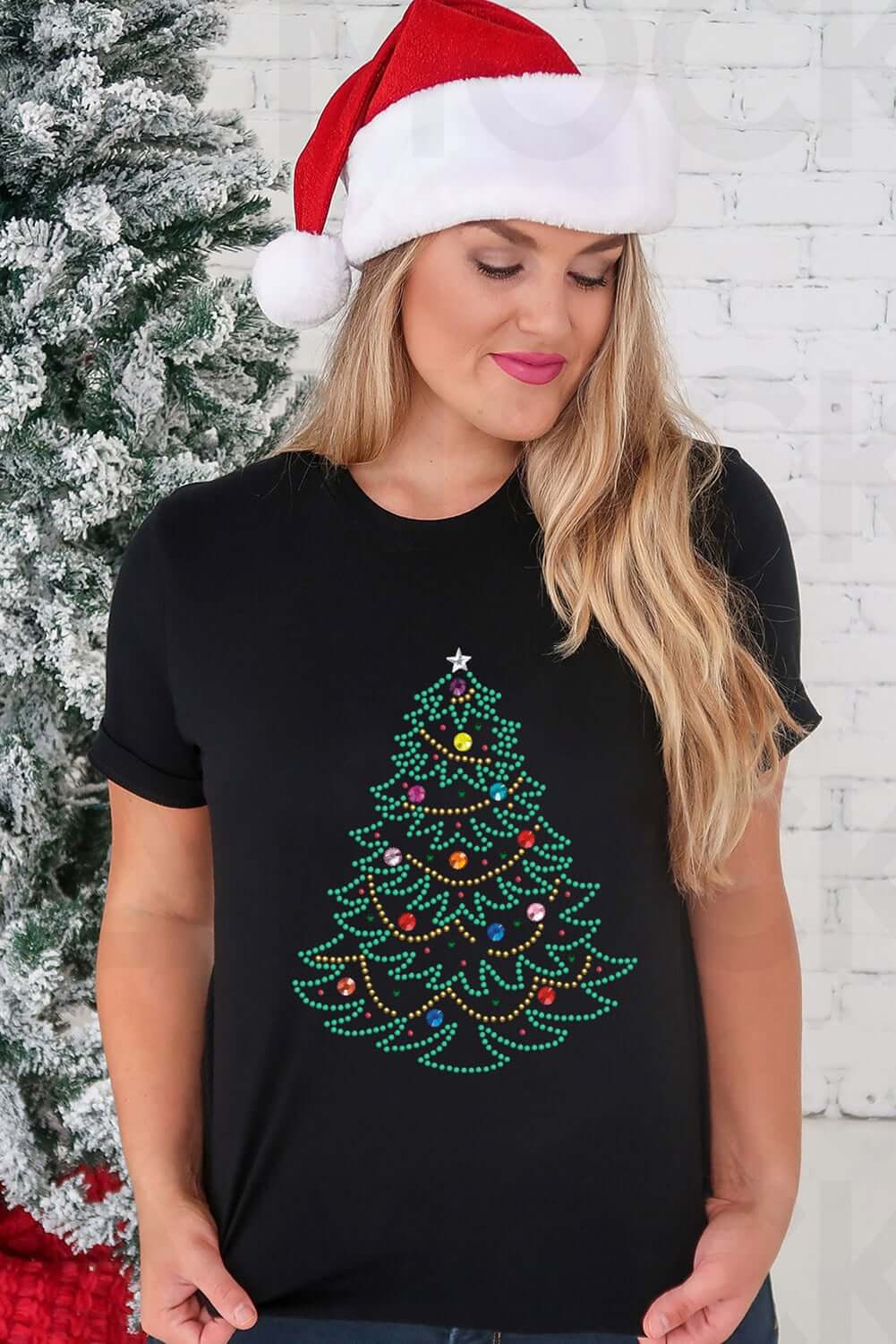 Woman wearing a black t-shirt with studded Christmas tree design, festive Santa hat, standing near a decorated tree.