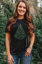 Woman wearing CHRISTMAS GEMS t-shirt with studded Christmas tree design, surrounded by evergreen trees.