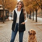 Model wearing REVERSIBLE RETREAT VEST (black) with coffee and dog in autumn setting.