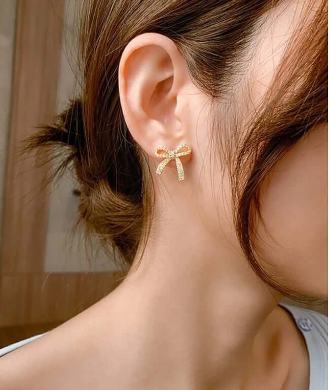 Elegant gold tone DAINTY BOW earrings by Vivian-Lu with rhinestones, worn by a model, perfect for elevating any outfit.