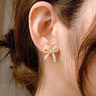 Elegant gold tone DAINTY BOW earrings by Vivian-Lu with rhinestones, worn in a woman's ear for a stylish look.