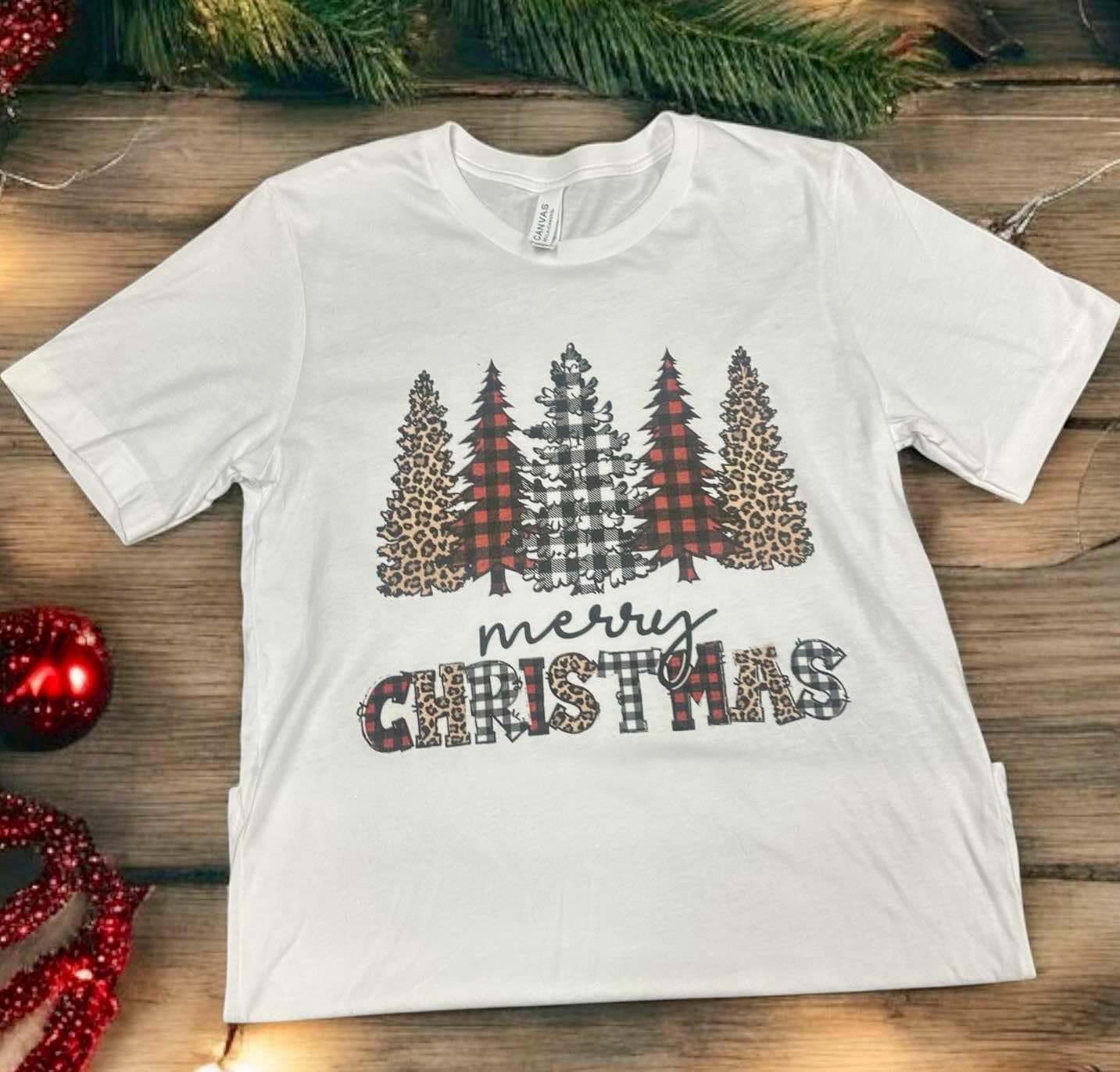 White Christmas tee with leopard and plaid tree design, featuring "Merry Christmas" text, festive holiday apparel by Bella Canvas.