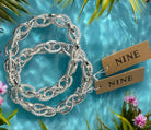 Silver stretch chain link bracelet by Nine Jewelry on tropical water background with flowers.