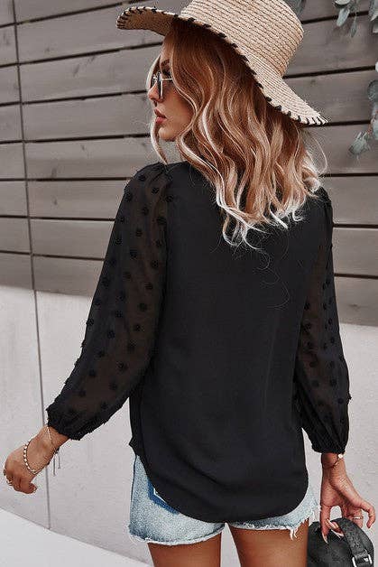 Back view of a woman wearing a black Swiss dot blouse with lantern sleeves and stylish hat.